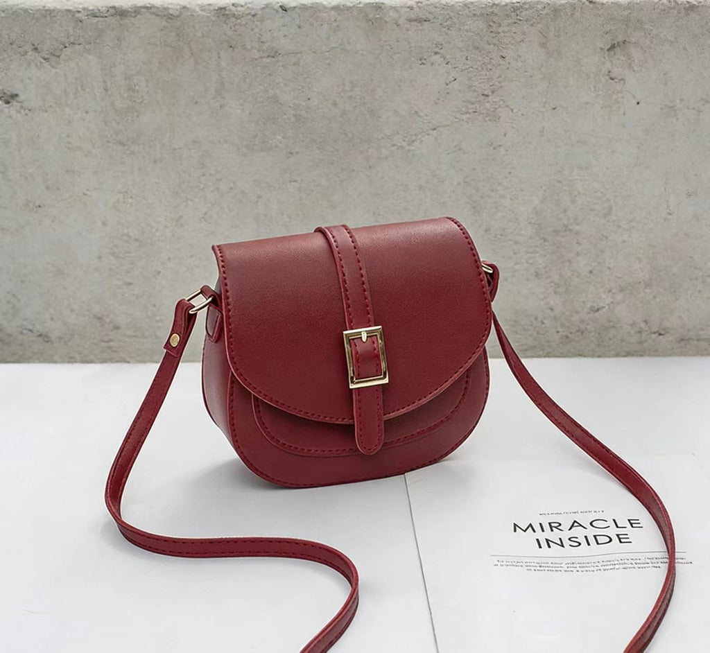 Simple metal-buckle flap crossbody saddle bag with an adjustable shoulder strap.