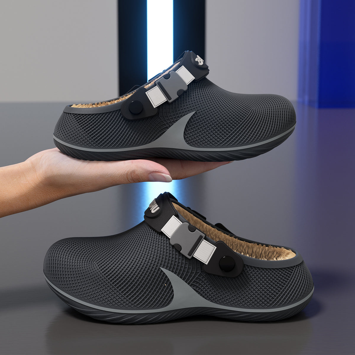 Two dark grey textured plastic slippers with tan fleece lining and adjustable straps held by a hand.