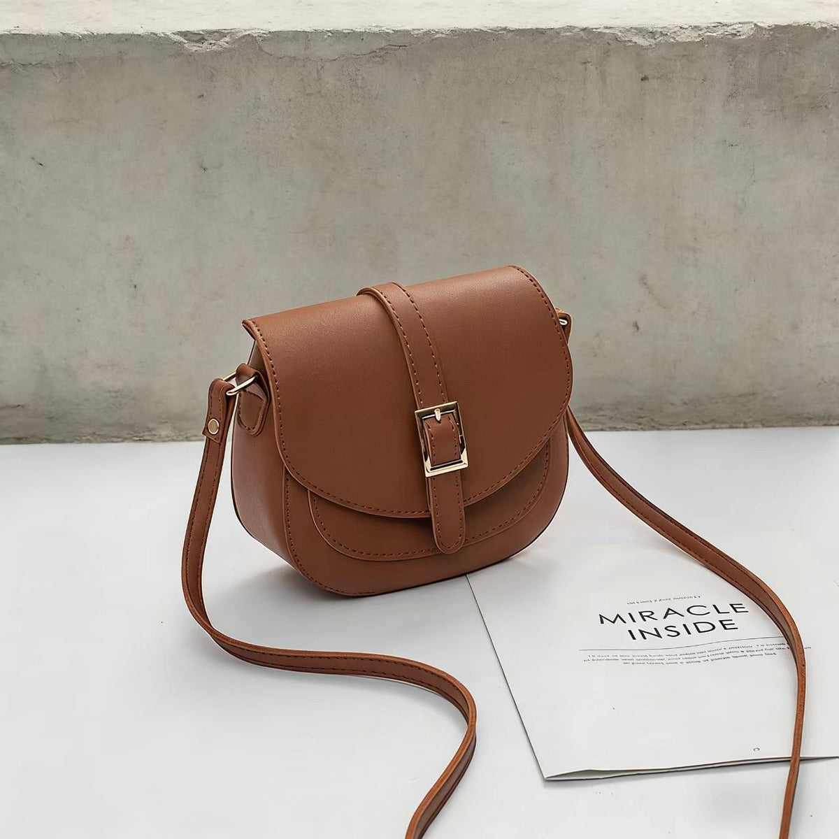 Simple metal-buckle flap crossbody saddle bag with an adjustable shoulder strap.