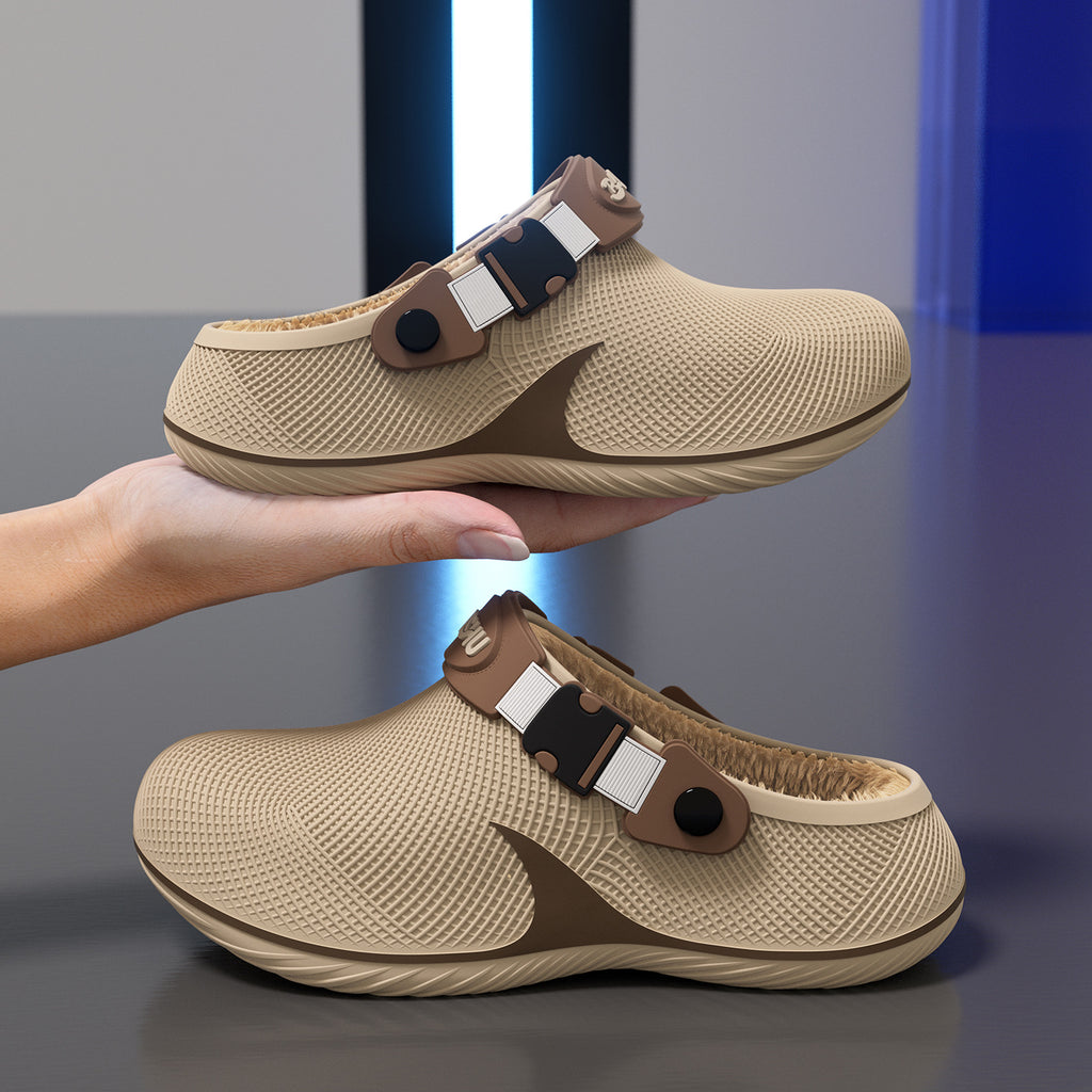 Two tan plastic slippers with fleece lining and buckled straps held by a hand against a gray and blue background.